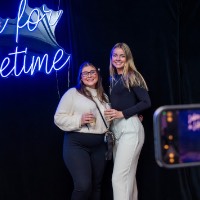 Two girls wearing black and white pose in front of Lakers for a Lifetime neon sign while someone takes their picture